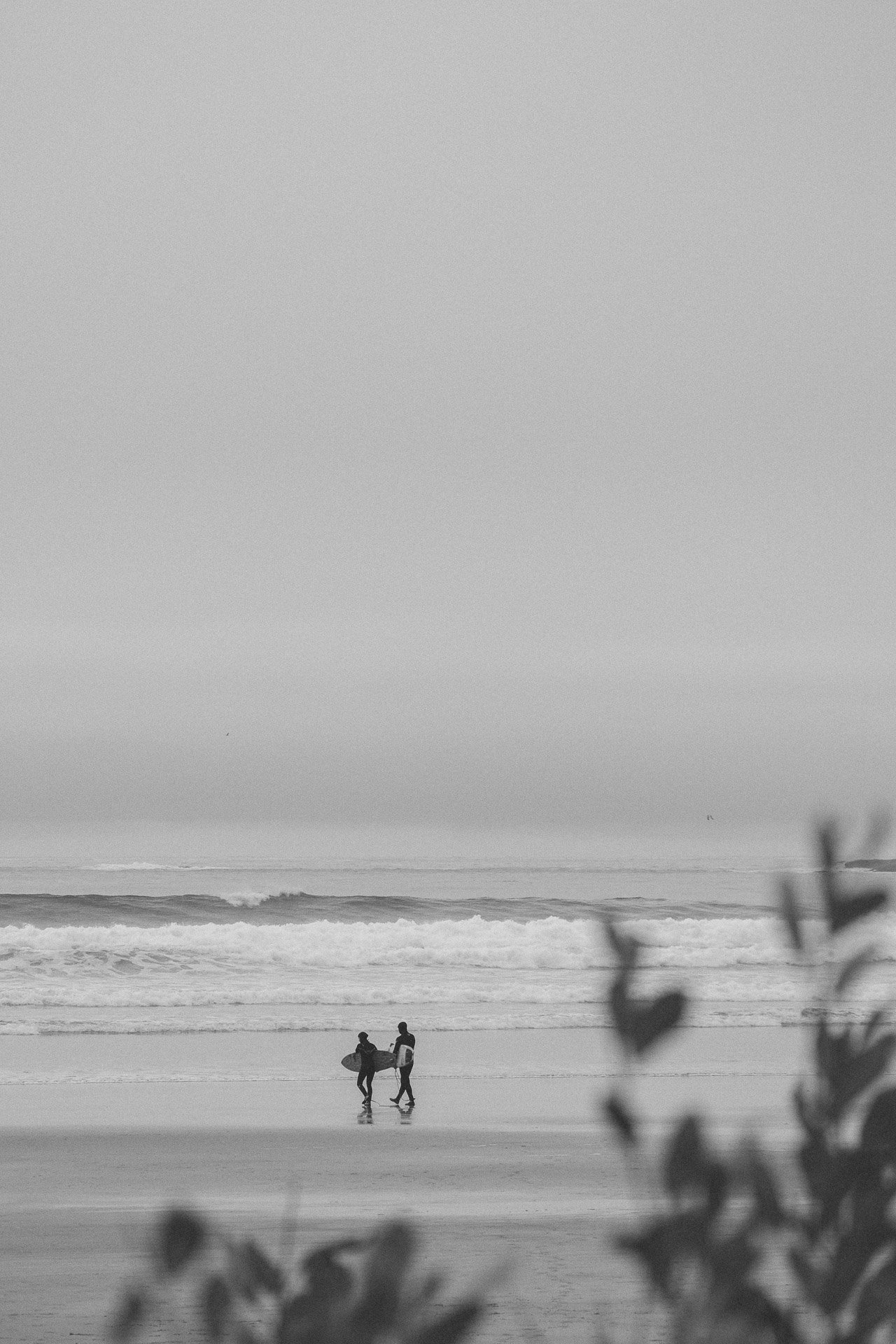 Twee surfers lopen met surfplanken over het strand