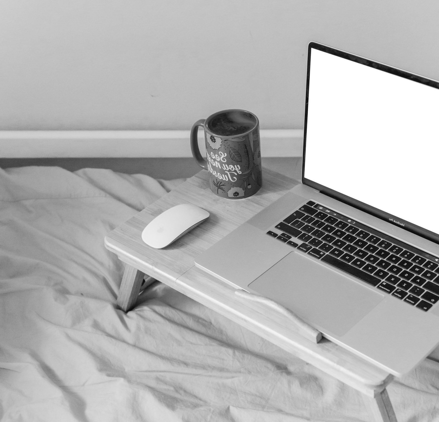 Laptop, kop koffie en muis op een bed