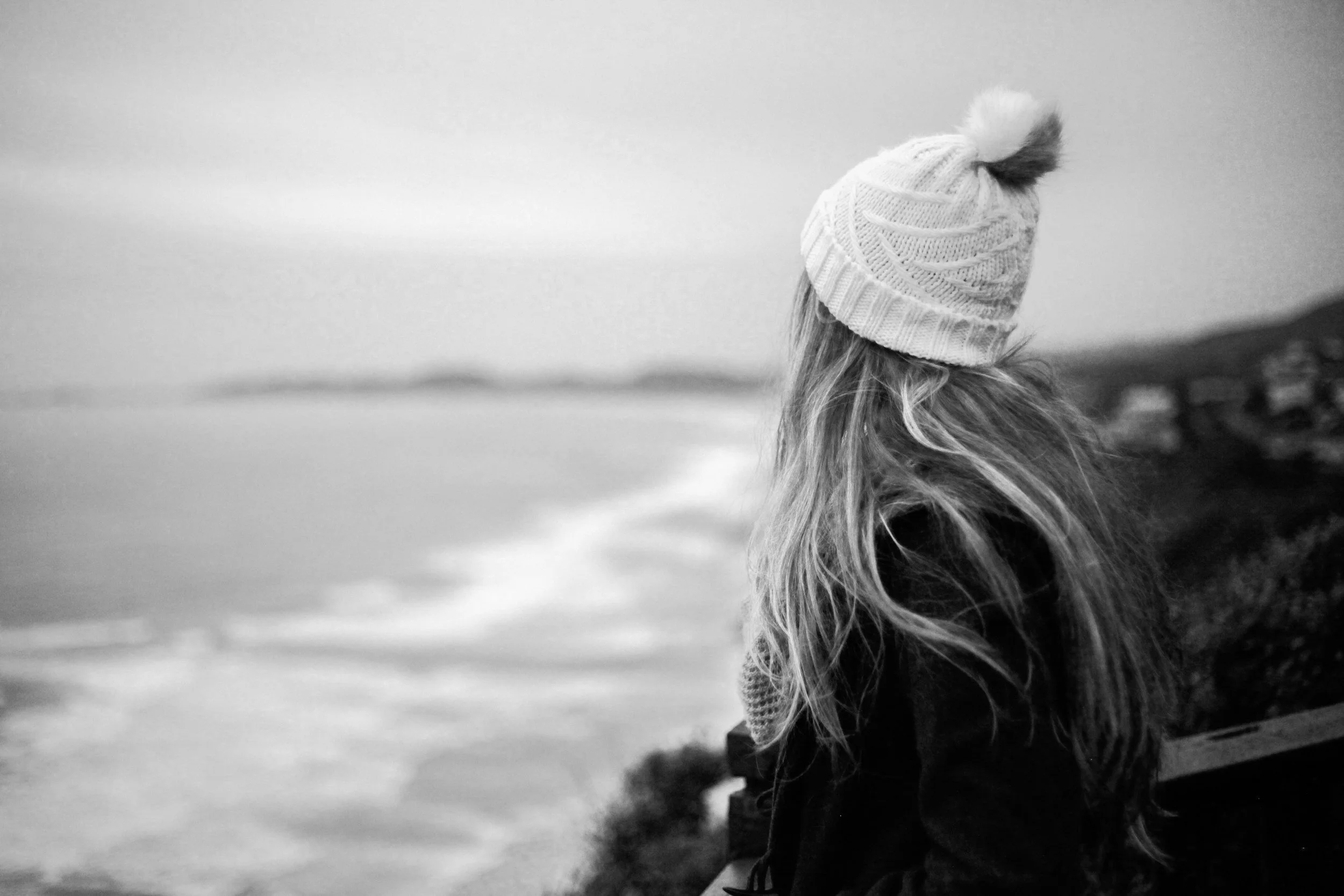 Persoon met een muts die uitkijkt over de zee