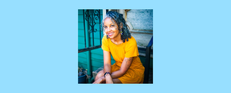 Dr. Michelle is a brownskin woman with salt and pepper hair in a bright yellow dress sitting on a porch with black iron door and green background. Photo by Nkechi Chibueze