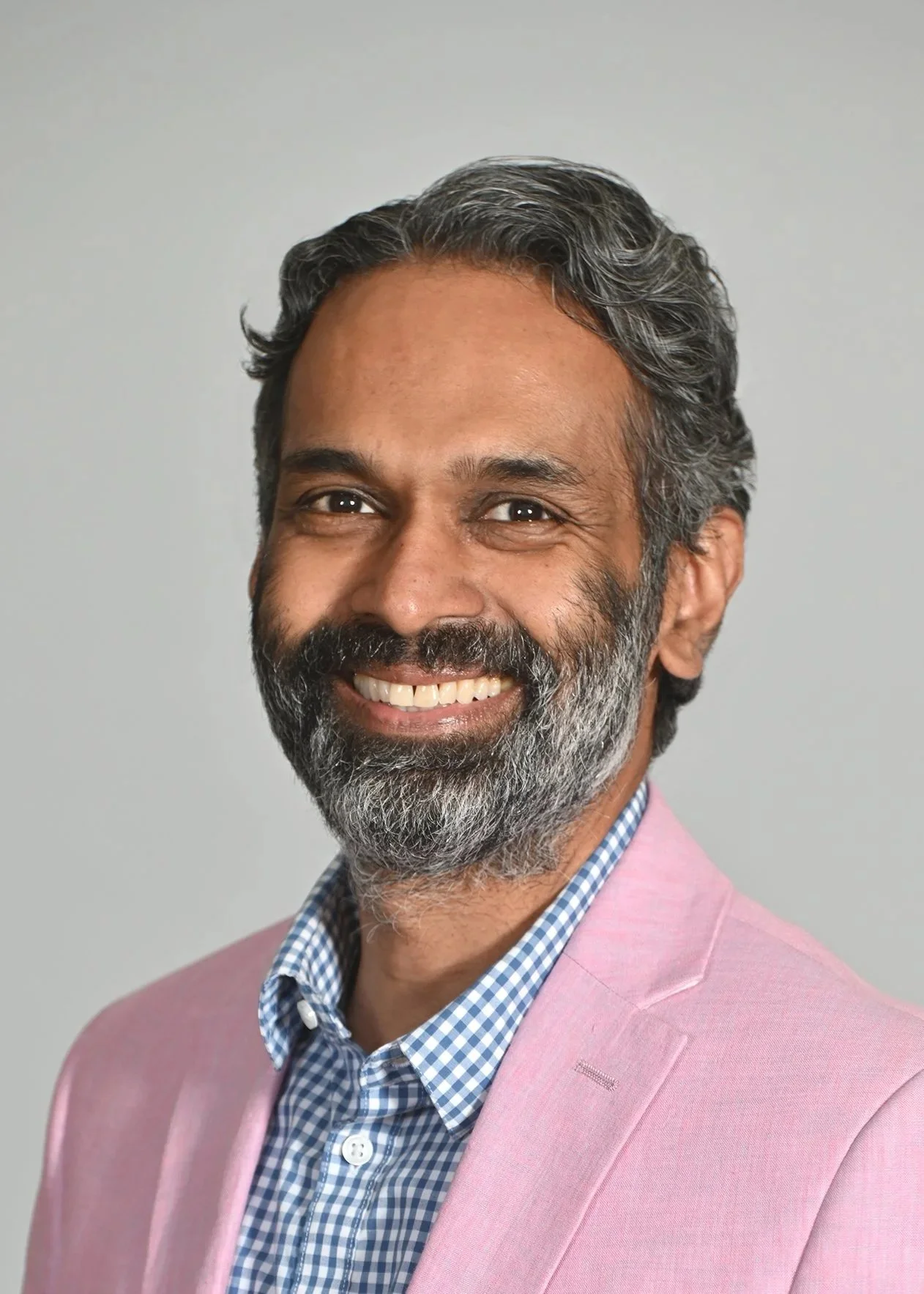 Daniel is smiling at the camera, he is wearing a dark blue shirt with rainbow hearts that signify queer pride