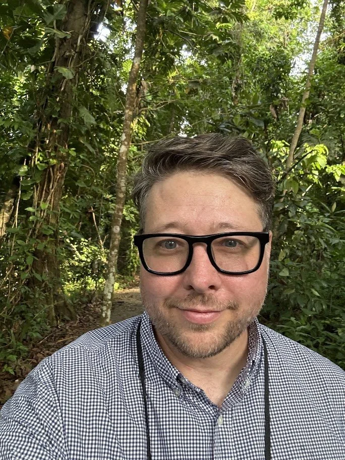 Ryan looking at the camera, with glasses wearing a blazer with a sculpture in the background