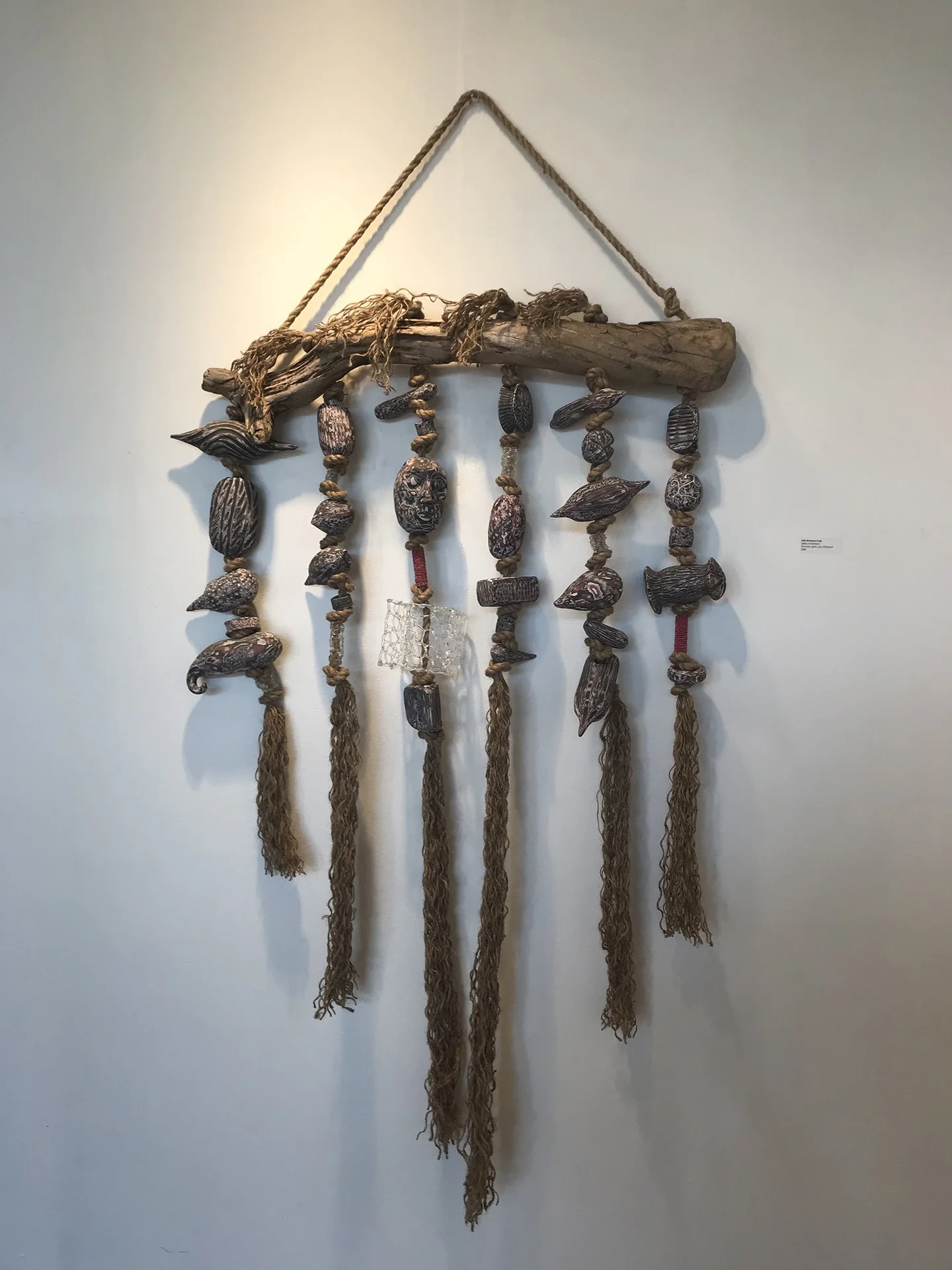 A wall hanging art piece made of driftwood, rope, and carved beads, resembling a dreamcatcher.