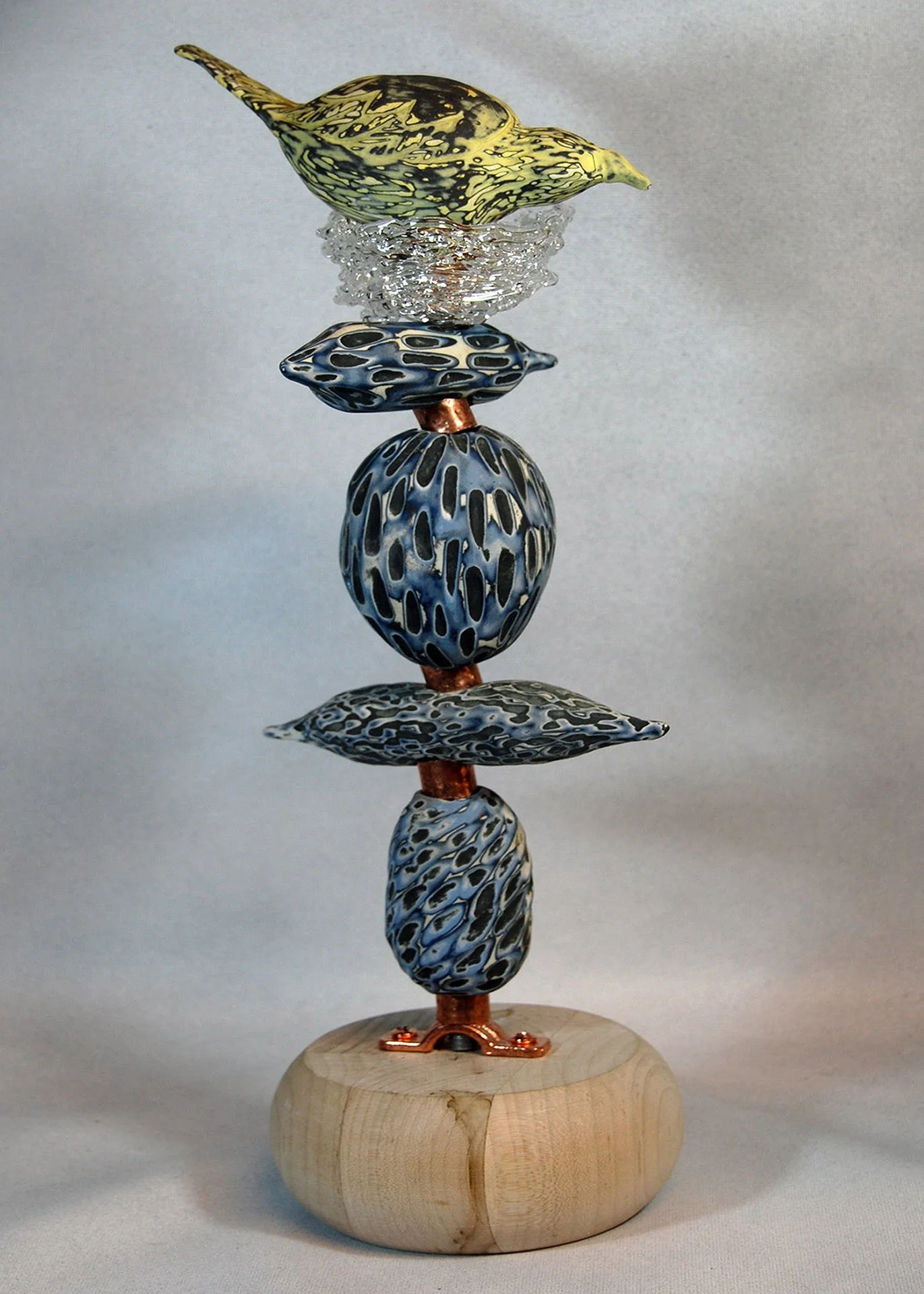 An abstract sculpture featuring a vertical arrangement of painted glass or ceramic forms stacked on a wooden base.