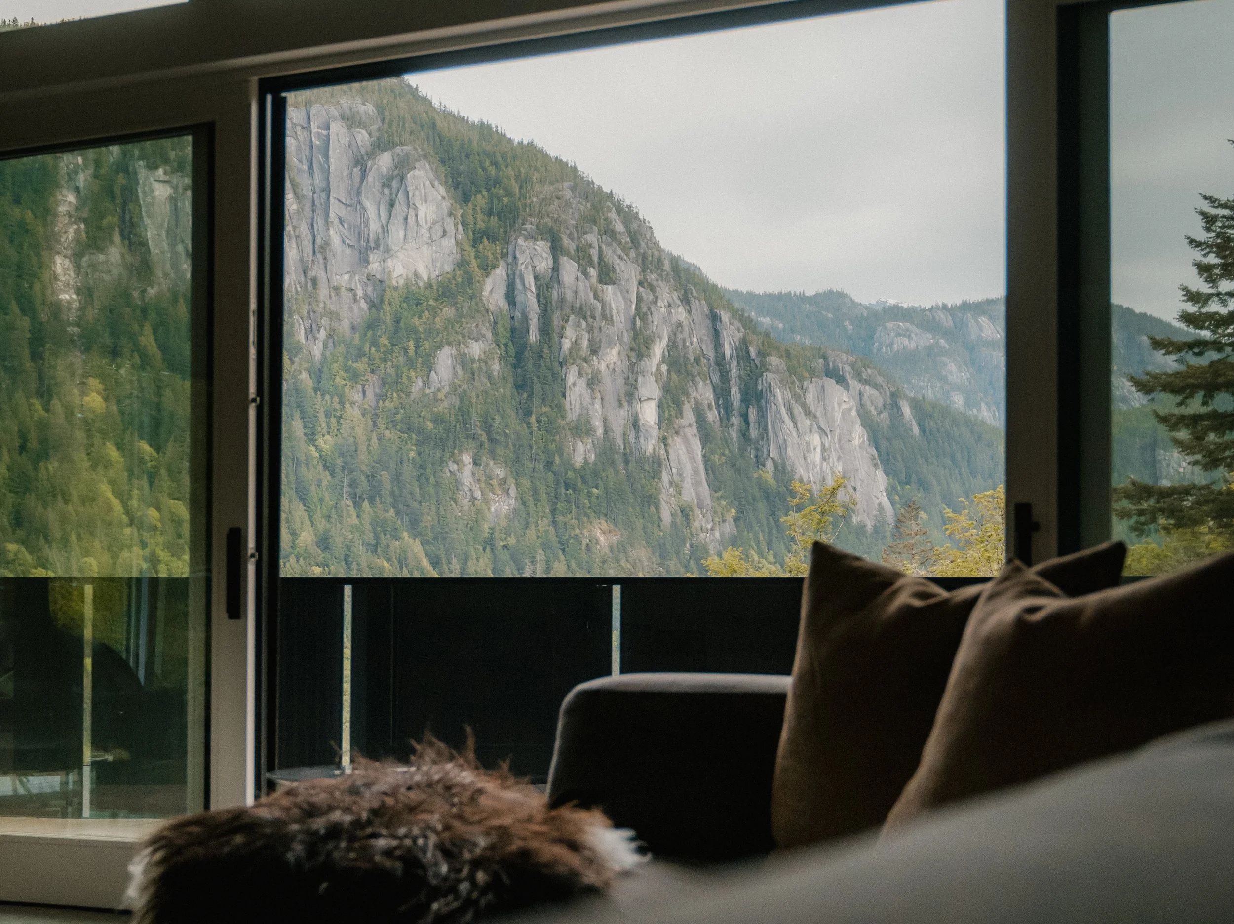 Living room with a large sliding glass door open to a mountain view with rocky cliffs and trees.