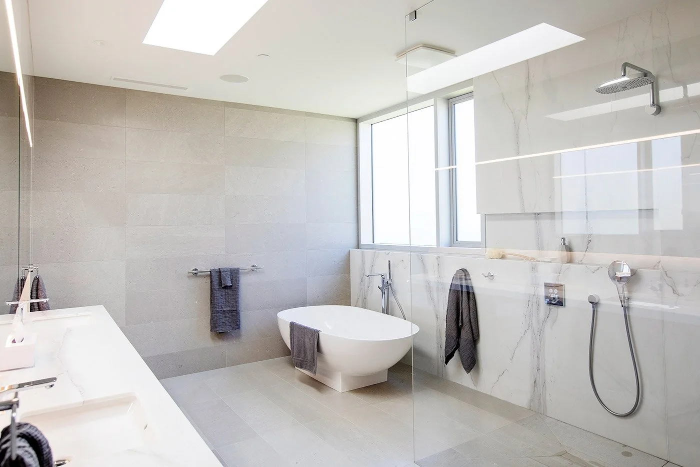 Modern bathroom with a freestanding bathtub, marble wall tiles, large window, and walk-in shower area.