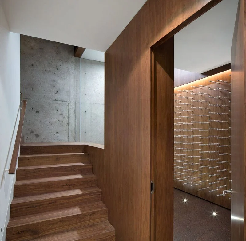 Interior of a modern home with wooden stairs, a concrete wall, and a wine cellar with a wood wall and wine racks.