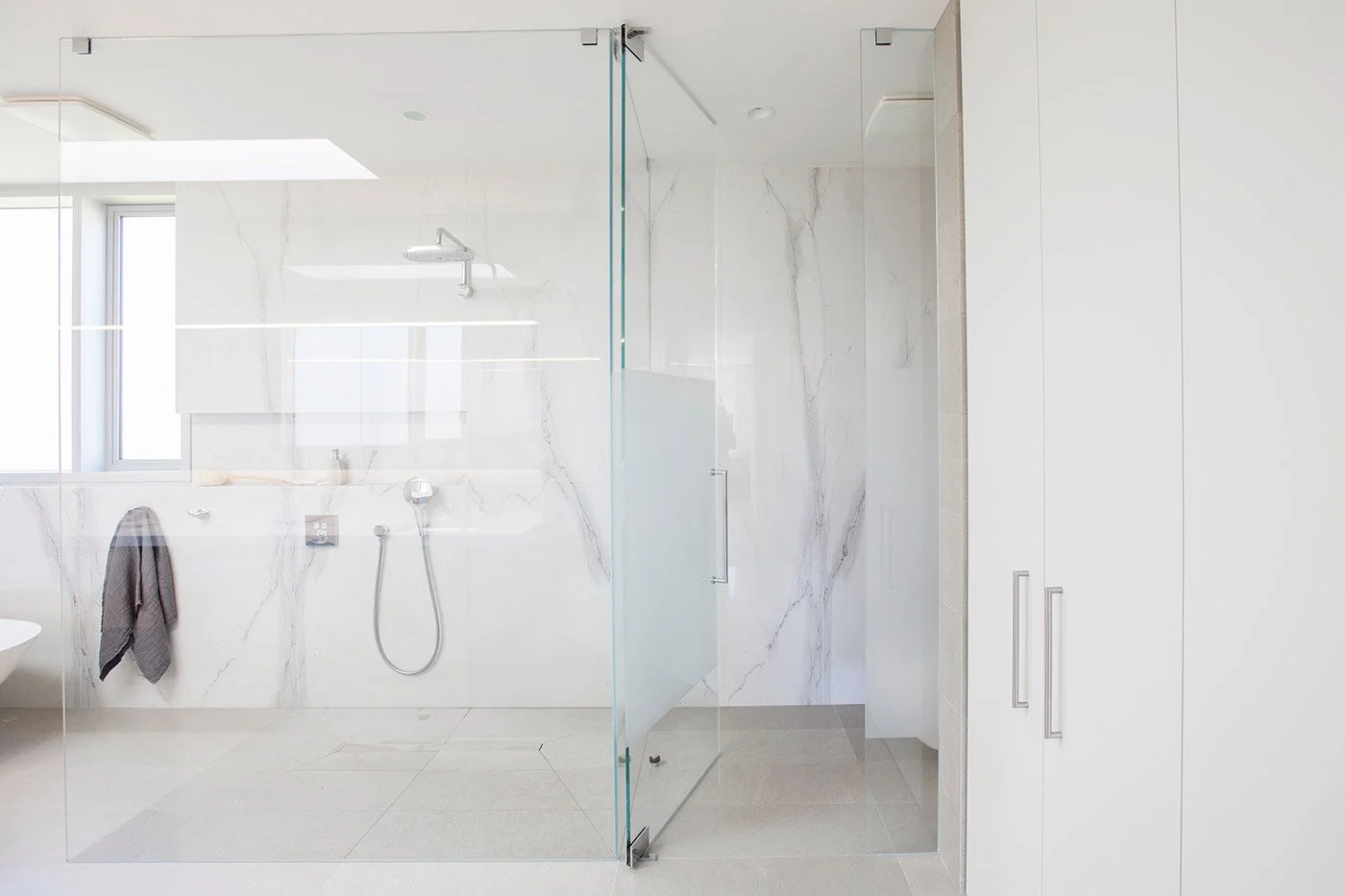 Modern white bathroom with marble walls and a glass shower enclosure.