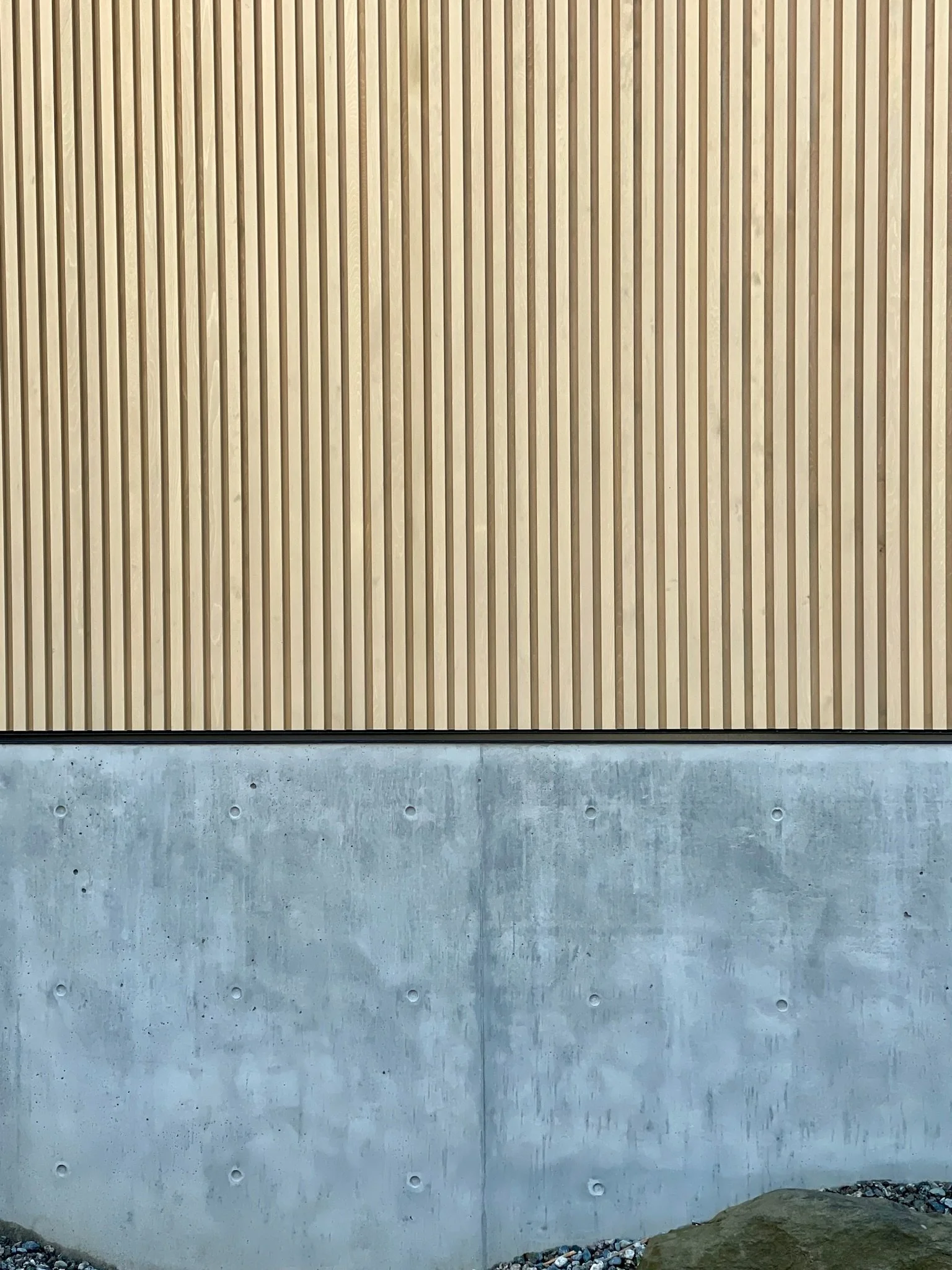 Photo of a wall with a concrete base and wooden vertical slat siding above.