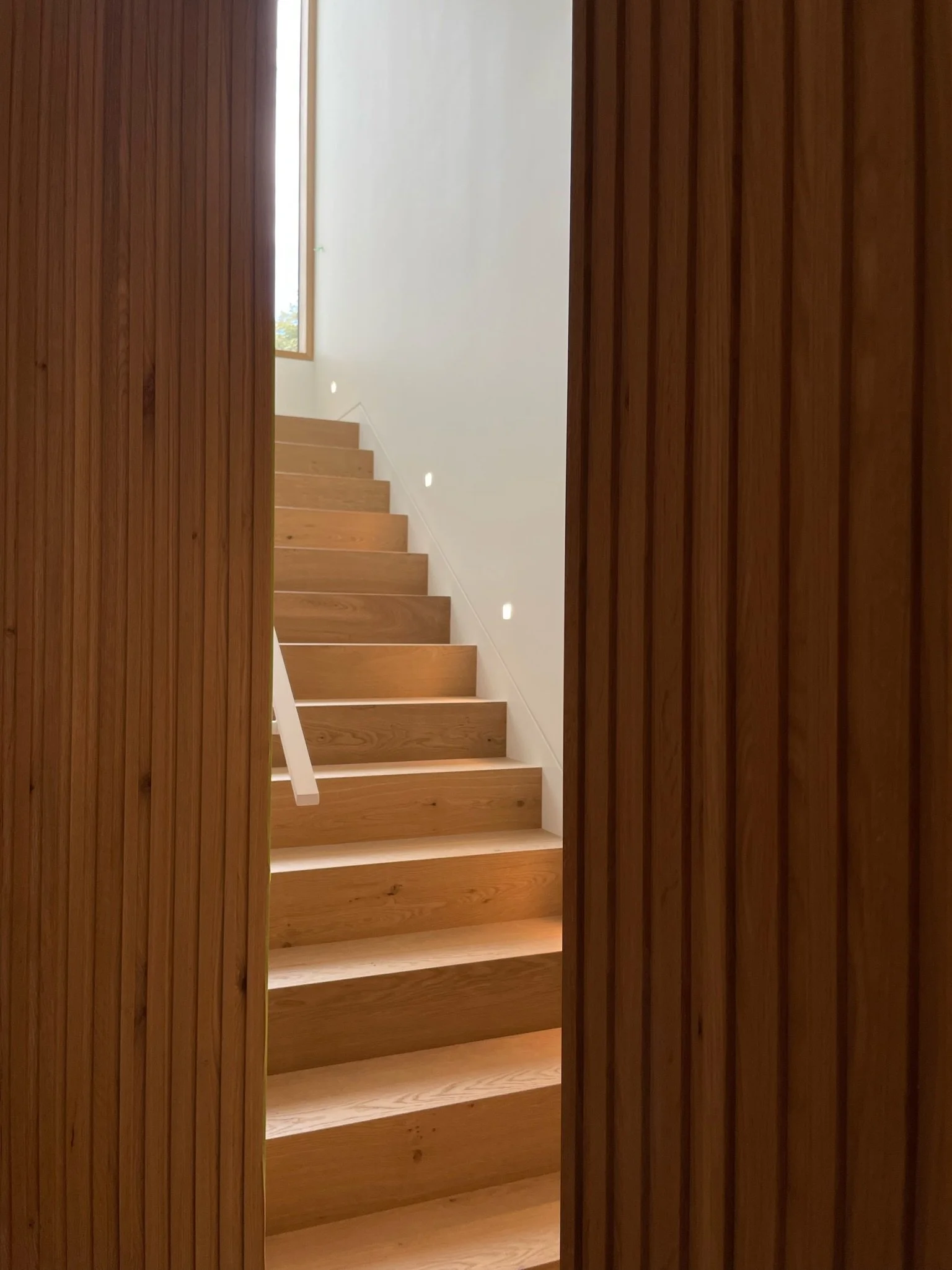 Wooden staircase viewed through doorway with vertical wood panel walls