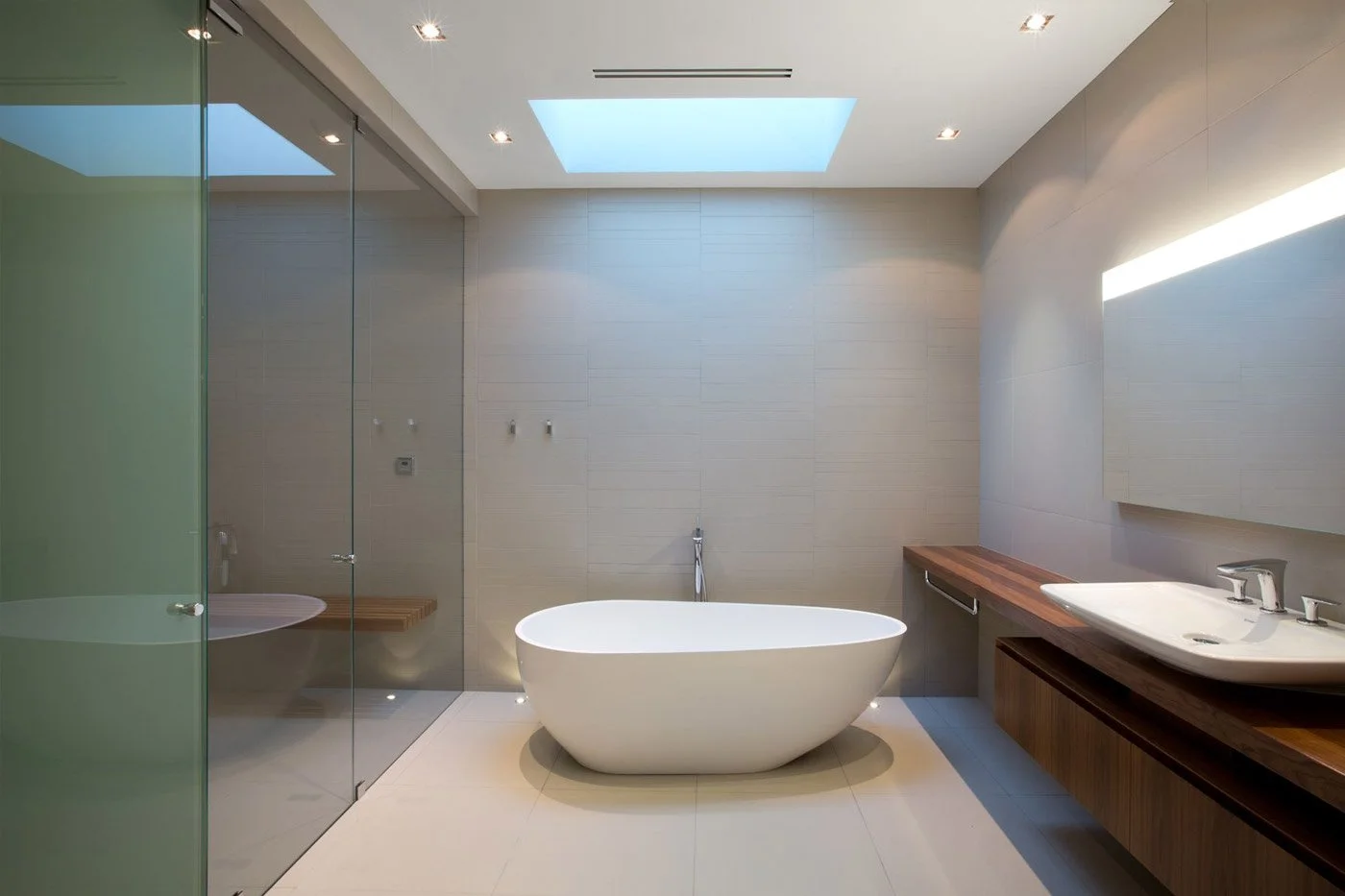 Modern bathroom featuring a freestanding bathtub, a wooden vanity with a vessel sink, a glass shower enclosure, and a skylight.