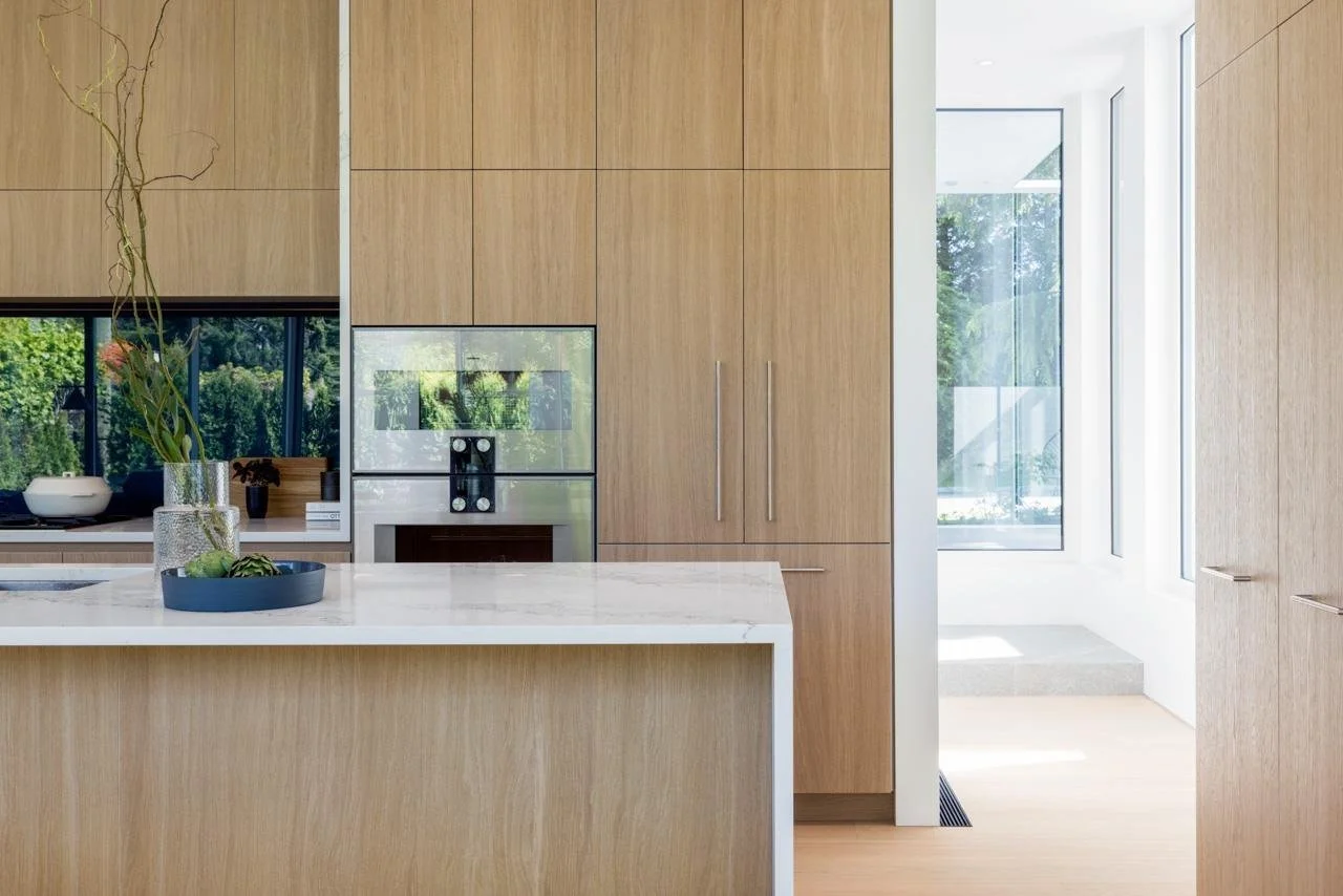 Modern kitchen with wooden cabinets, white marble island, and large windows letting in natural light.