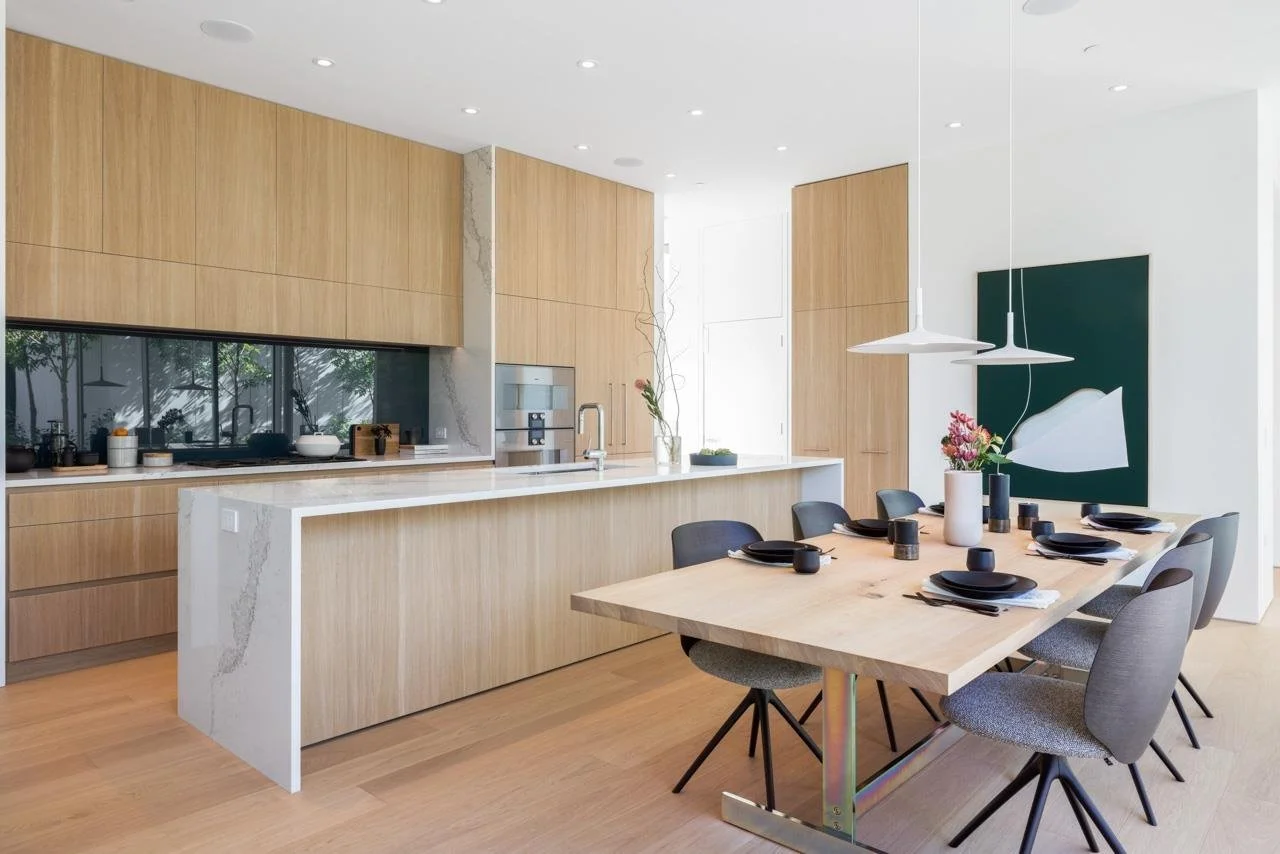 Modern open-concept kitchen and dining area with wooden cabinetry, white marble island, black dining chairs, and minimalist decor.