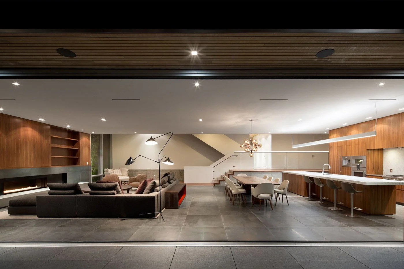 Modern open-concept living room and kitchen with wood accents, a black sectional sofa, and a dining area with white chairs.