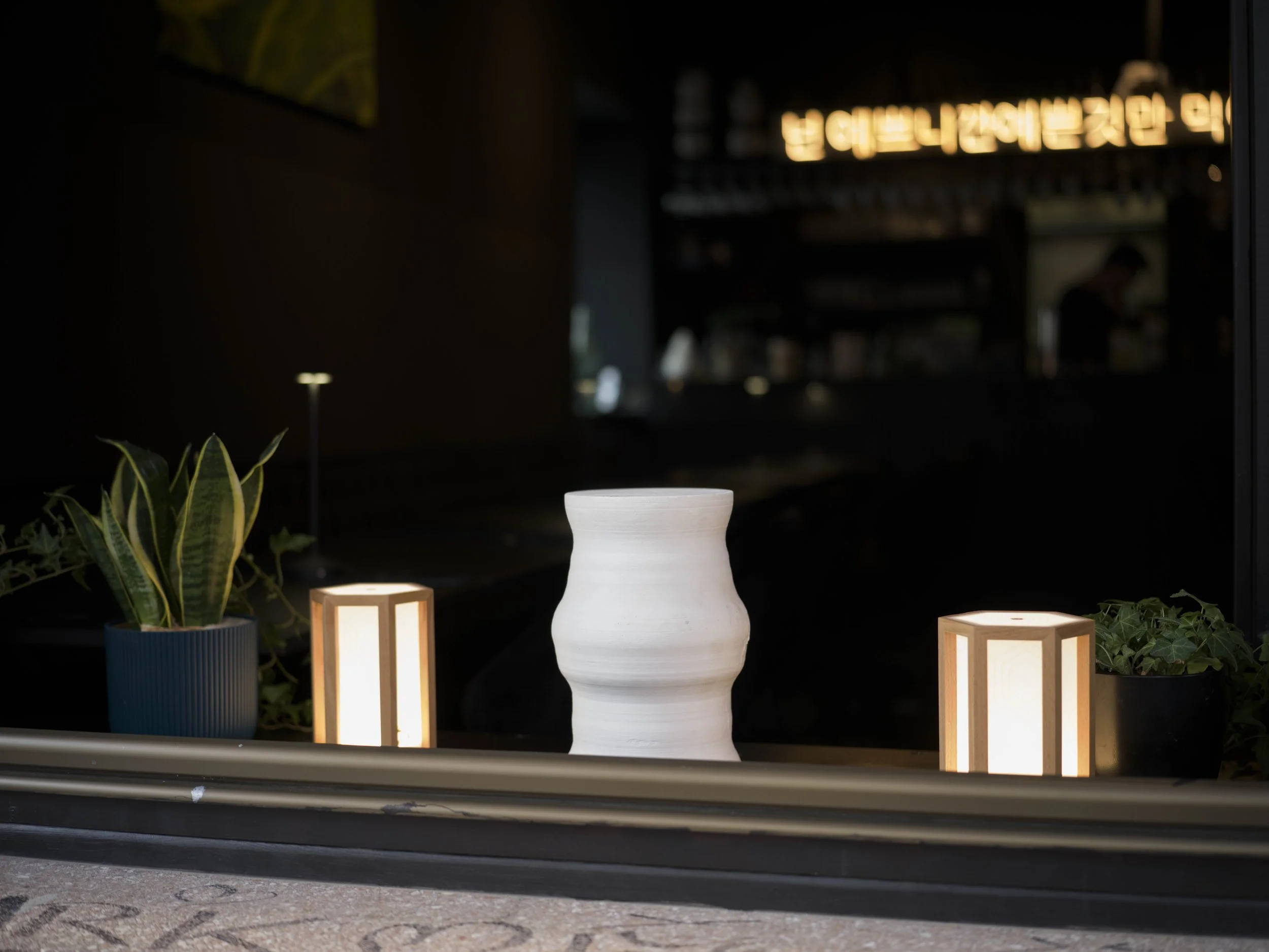 Fensterdekoration mit zwei Pflanzen in Töpfen, zwei leuchtenden Lampen und einer weißen Vase, im Hintergrund das Interieur Neonbeschilderung.