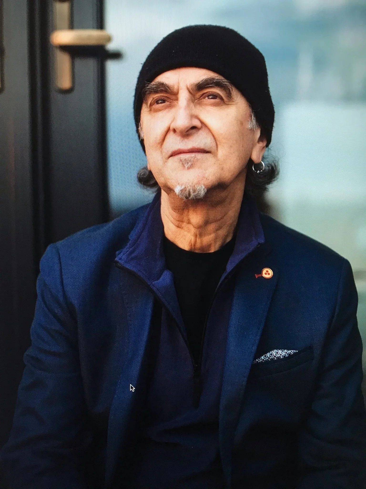 Close-up of an older man with a black beanie, earrings, and a blue jacket.