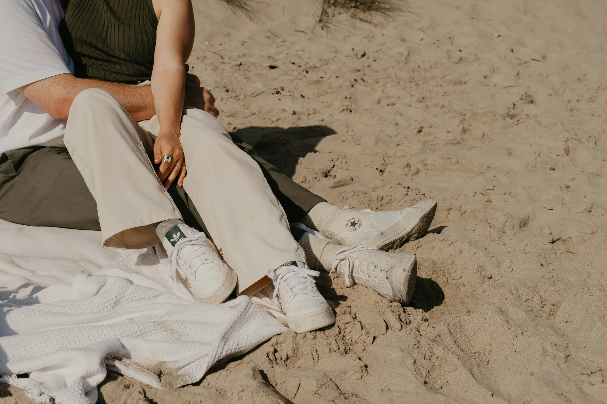 Close-up of couple sitting close on a sandy beach, their bodies relaxed and connected — evoking grounded intimacy and emotional presence