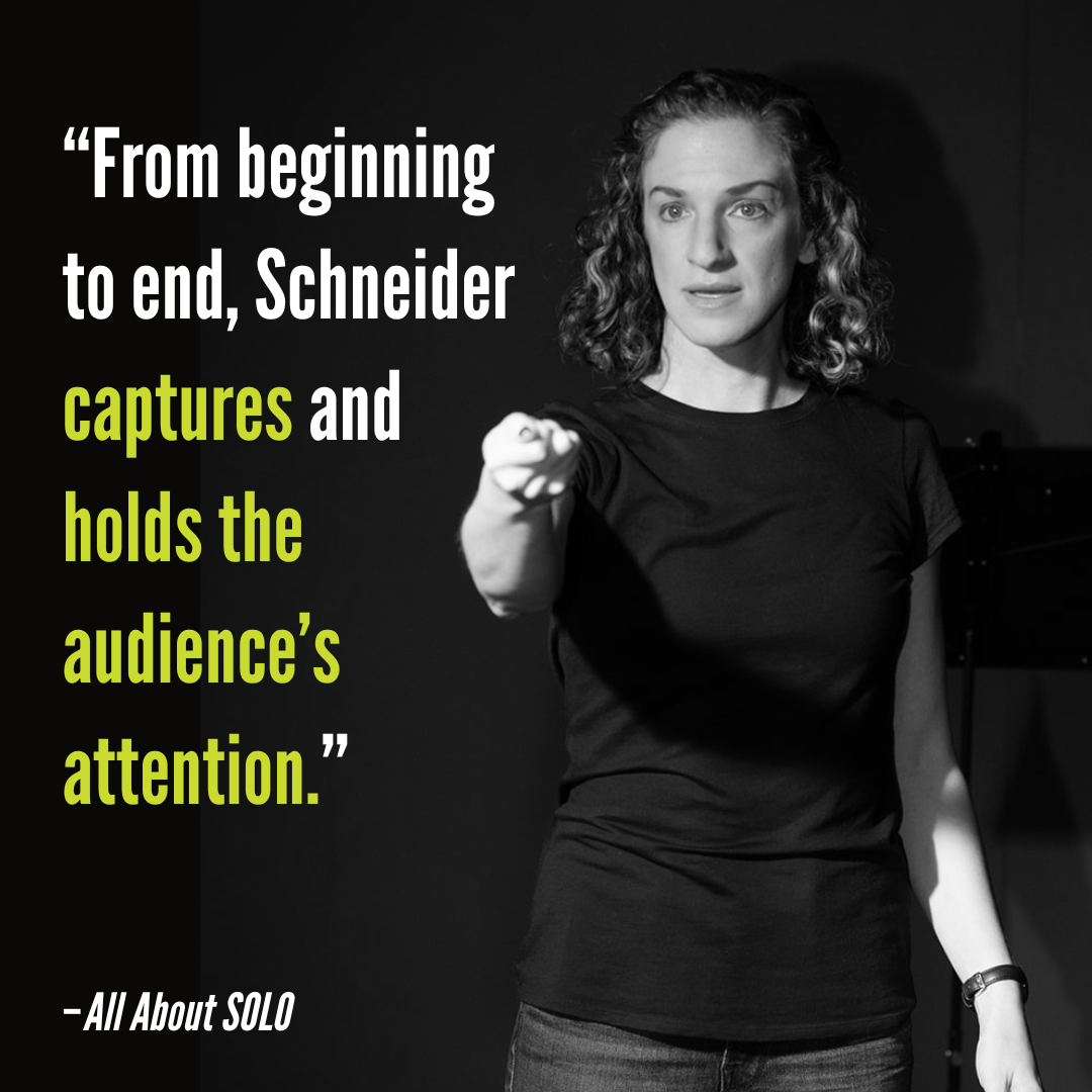 Black and white photo of a woman with curly hair, wearing a black shirt, speaking and pointing forward onstage. Overlaid quote: 'From beginning to end, Schneider captures and holds the audience’s attention.'