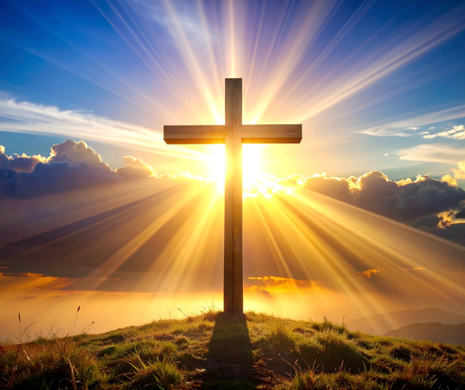 Wooden cross on a hill with the sun shining behind it, creating rays of light in the sky.