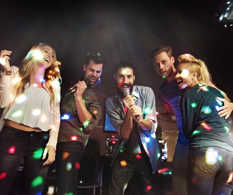 Group of five young people singing and dancing at a party with colorful lights.