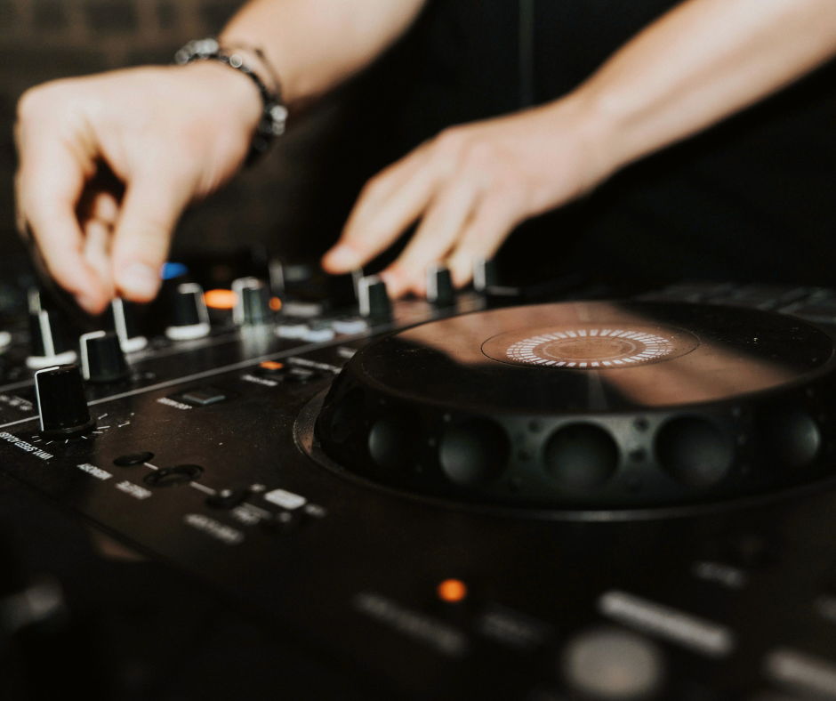 Close-up of a DJ using a mixer and turntable with hands adjusting controls.