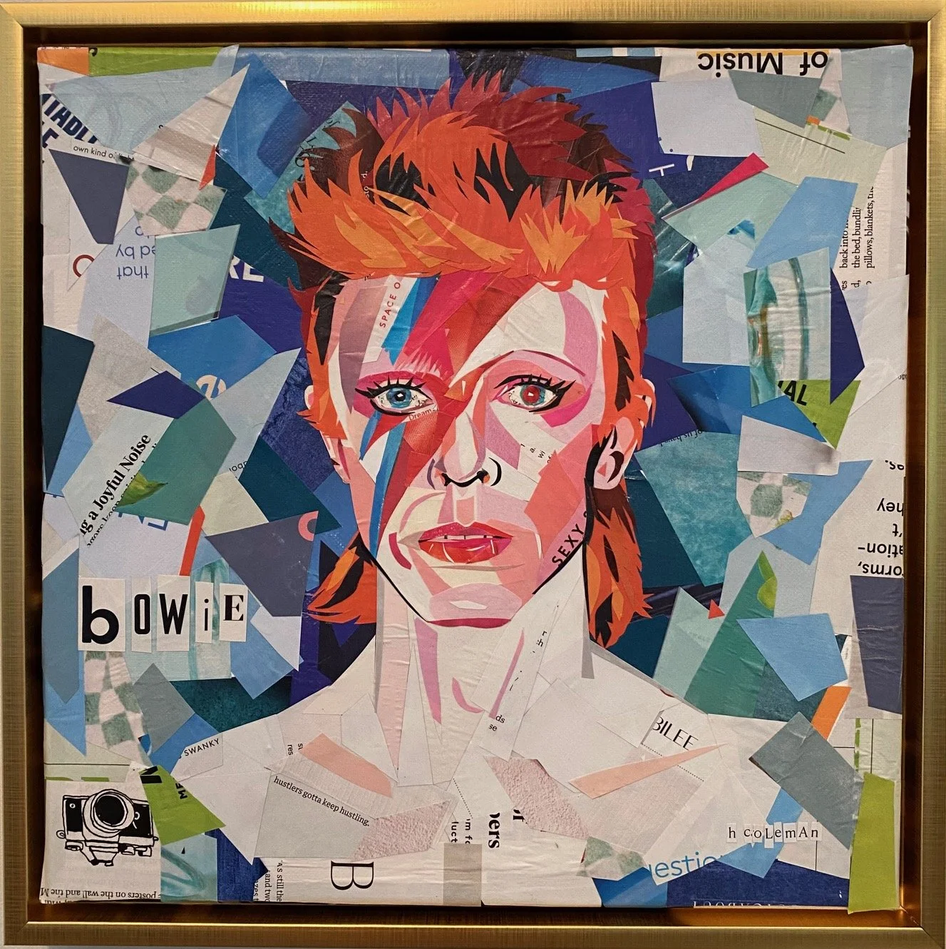 Collage of David Bowie portrait created with cut-out magazine paper pieces, framed. The portrait features Bowie with red hair, striking eye makeup, and an intense gaze. The collage includes text snippets and images layered to form his face and hair, 