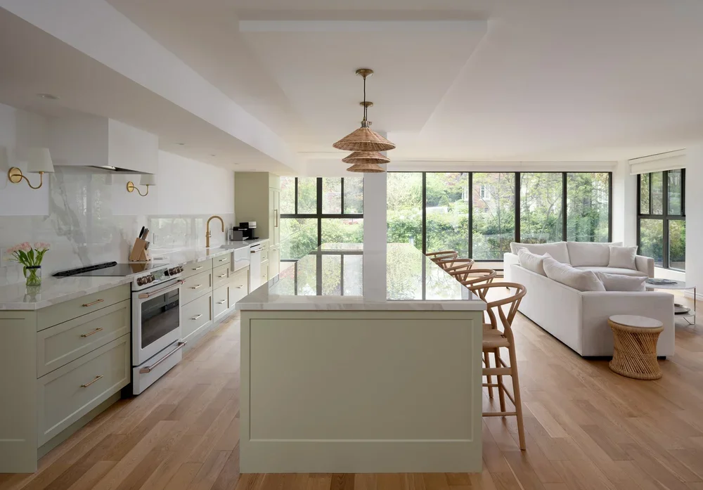 Open concept condo kitchen and living room. Soft mint green cabinets, island with eat up bar stools, open to living room with floor to ceiling windows.