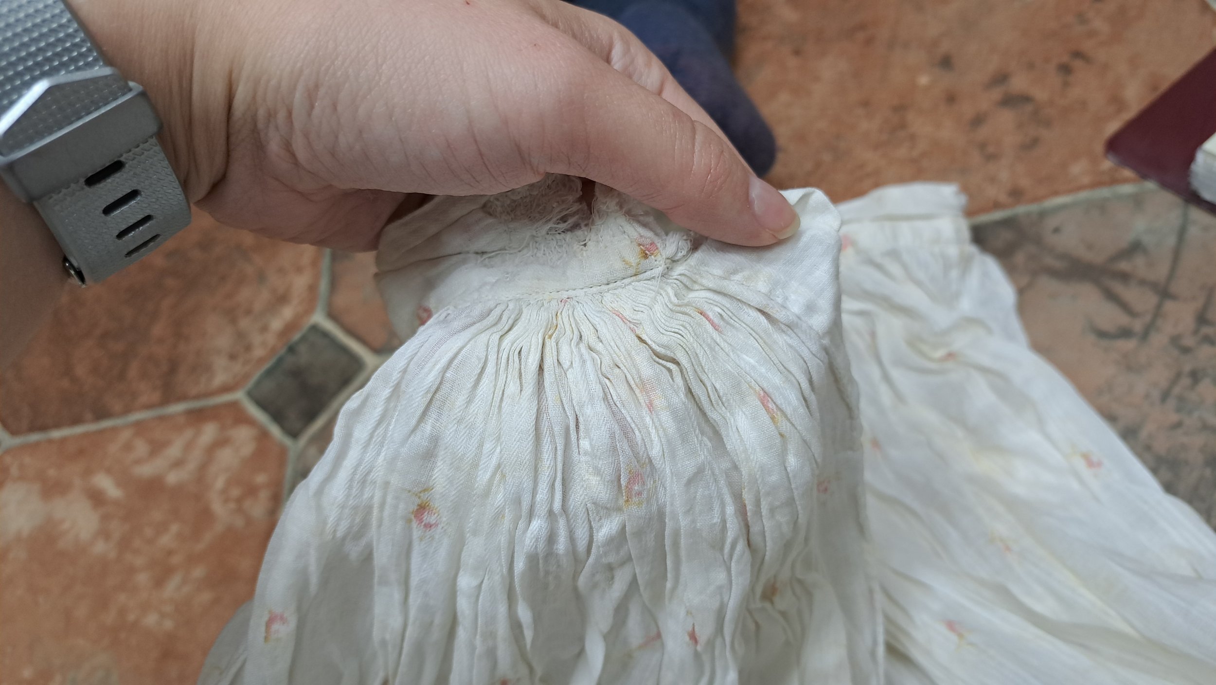 The original placket on the 1897 skirt. A woman's hand holds the piece from the top, showcasing the cartridge pleats and the placket pinched between her thumb and fingers.