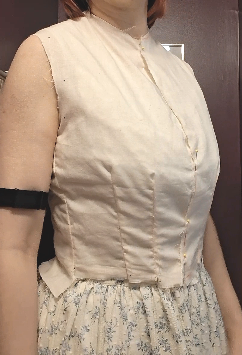 A close-up side view of Kyla wearing a fitted muslin fabric mockup of an 1890s Keystone Waist bodice lining pinned down the front.