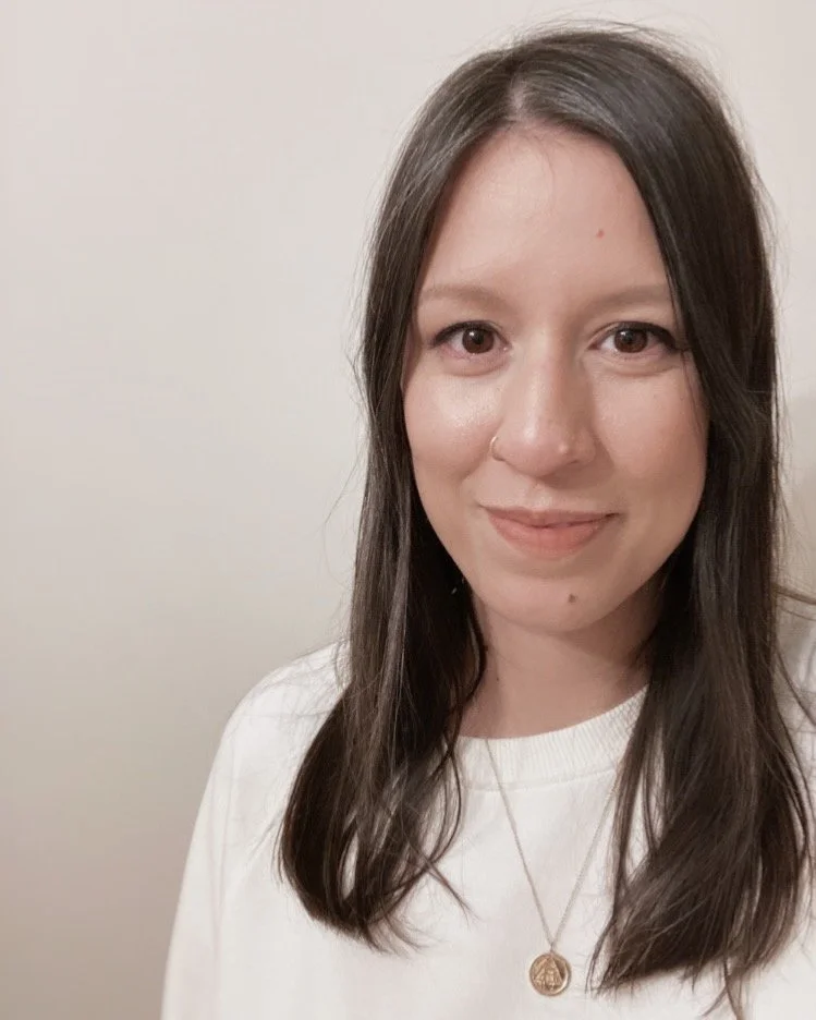 Nash Gierak, founding director of Bold Green Strategies sustainability consultancy. A woman with long brown hair, smiling in front of a plain beige wall, wearing a white shirt and a gold necklace with a pendant.