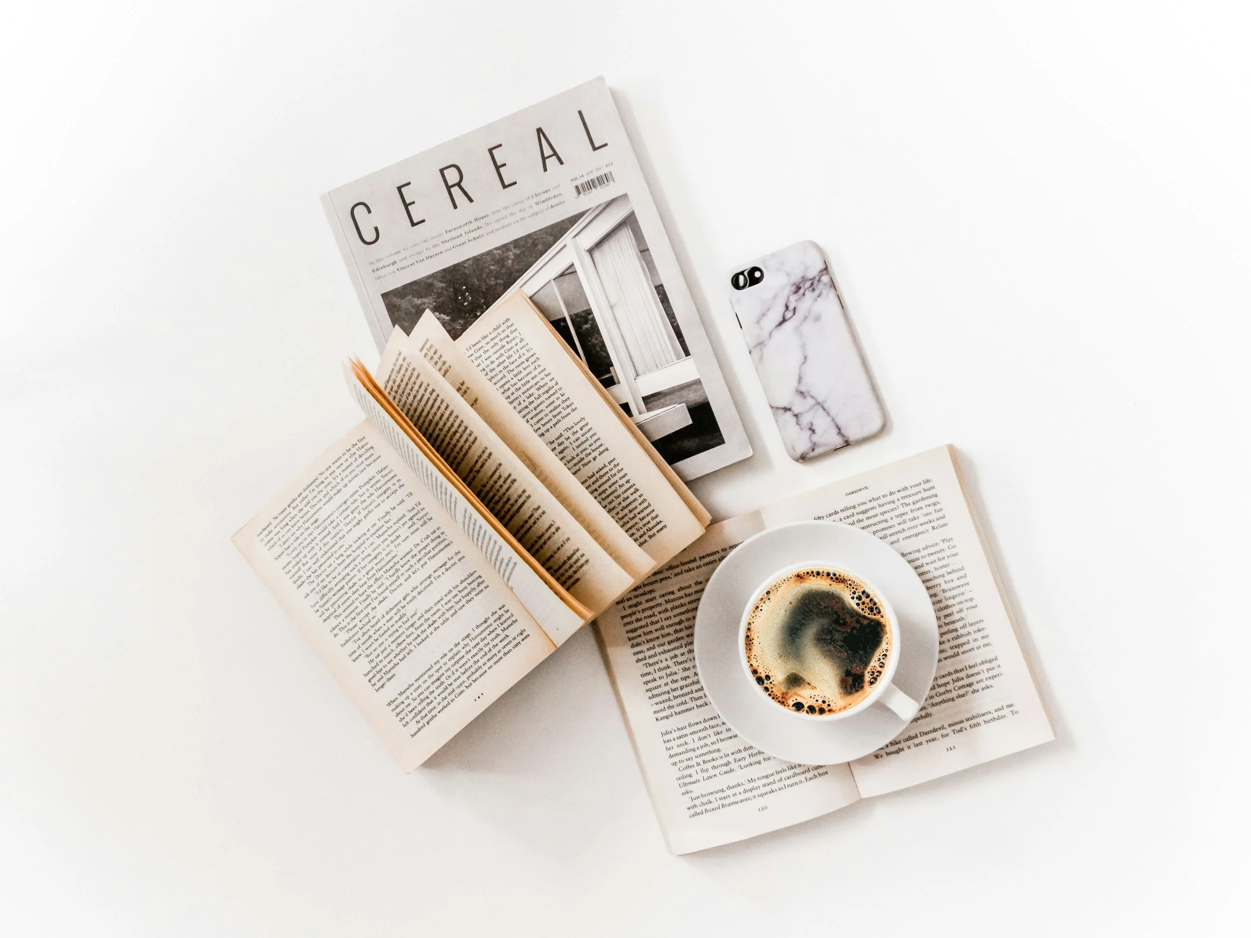 A minimlaist flatplay of open bools, a copy of Cereal magaize, a black coffee in a cup representing stakeholder facing narrative and storytelling for luxury brands and services.