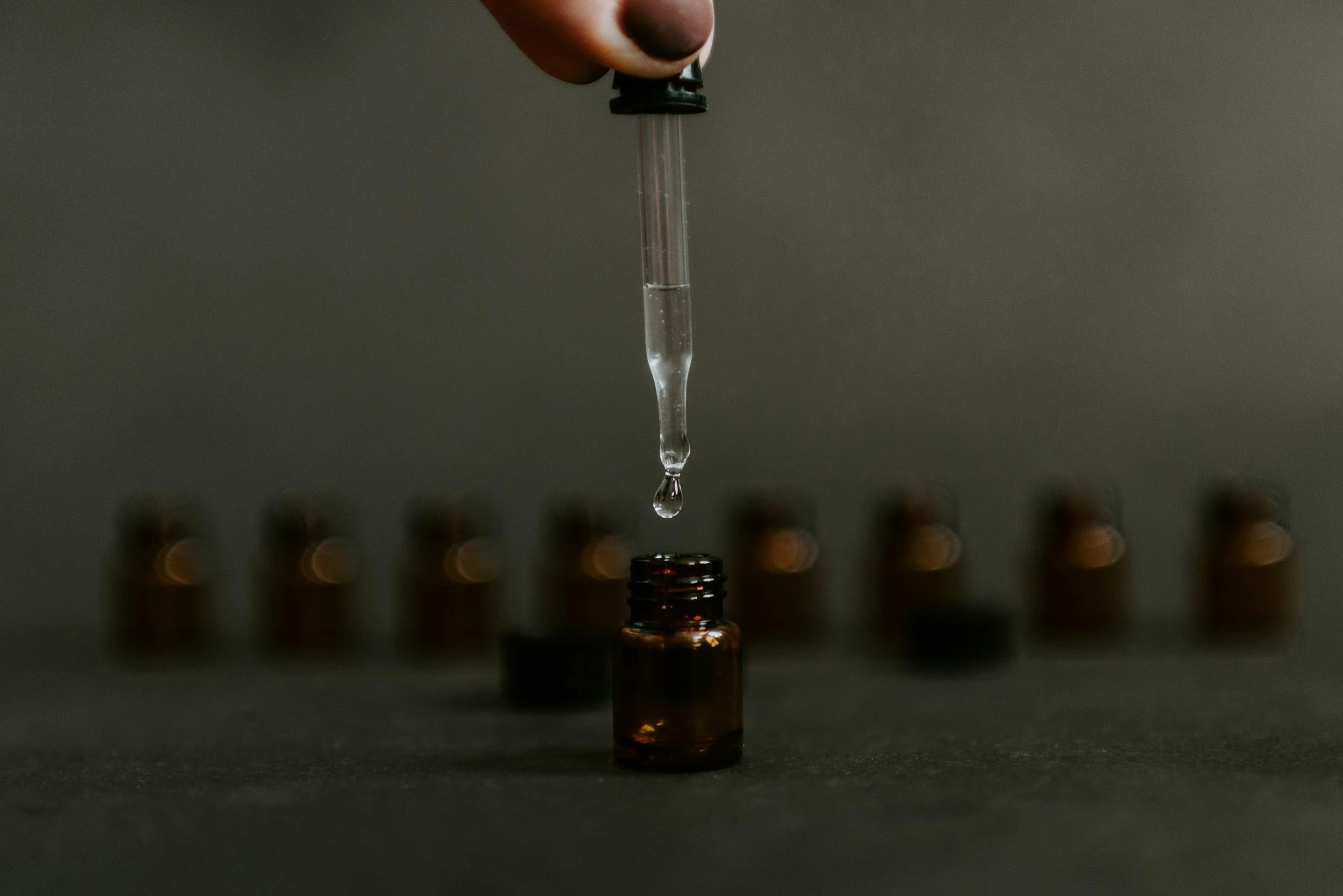 A pipette dropping liquid into an amber glass bottle representing the materiality deep dives and supply chain work the consultancy does.