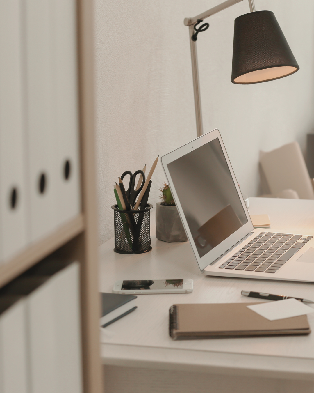 A laptop on a desk with a pen pot and files on a bookcase. This represents the consultancy's collaborative design and advisory role.