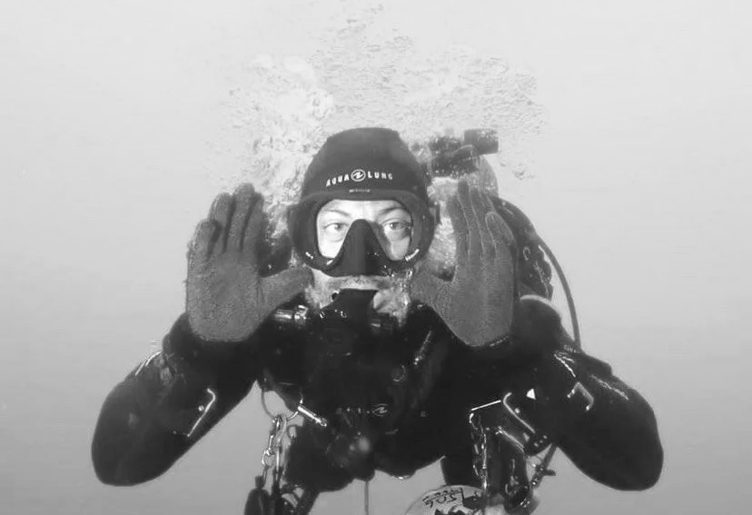 Scuba diver underwater making a sign with hands near face