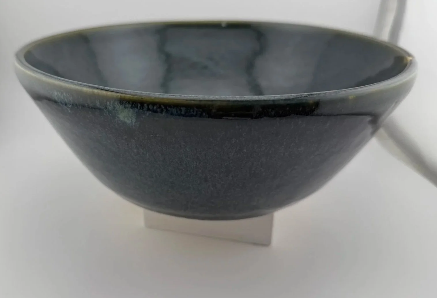 Dark gray ceramic bowl with a glossy finish, resting on a small white stand, against a white background.