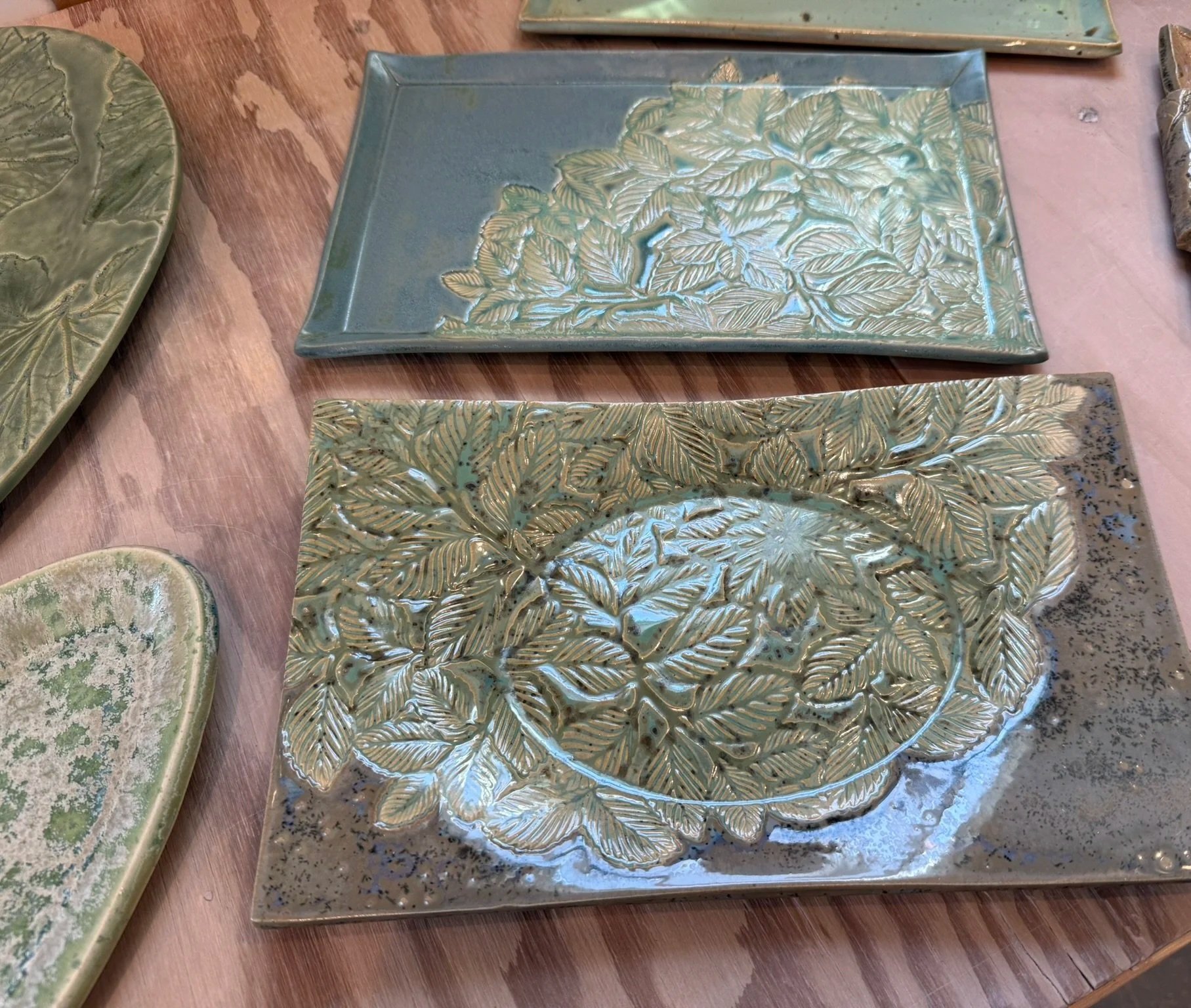 Ceramic plates with leaf and Branch patterns, one rectangular and one oval, in shades of green and blue on a wooden table.