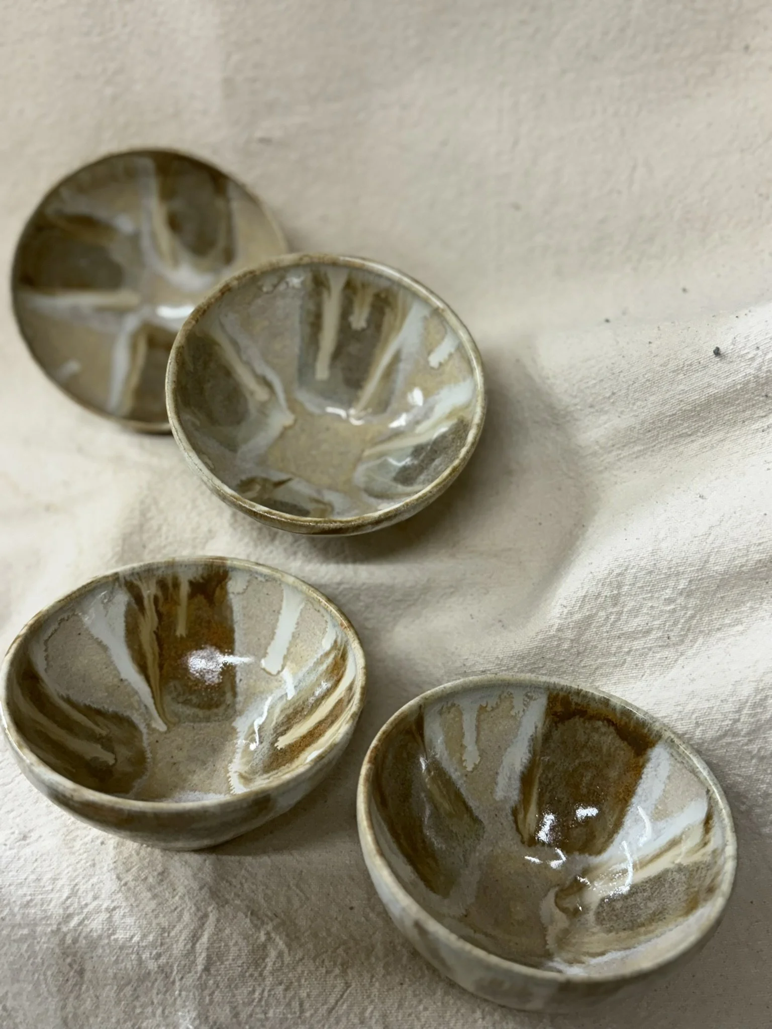 Four small ceramic bowls with a beige and brown marbled pattern, placed on a white textured surface.