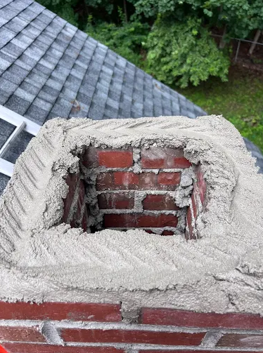 Brick chimney crown repair in progress with fresh mortar applied around the flue, showcasing professional chimney repair and masonry restoration services by Granite State Chimney.