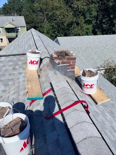 Brick chimney repair in progress on residential roof with masonry materials and tools, showcasing professional chimney repair and restoration services by Granite State Chimney.