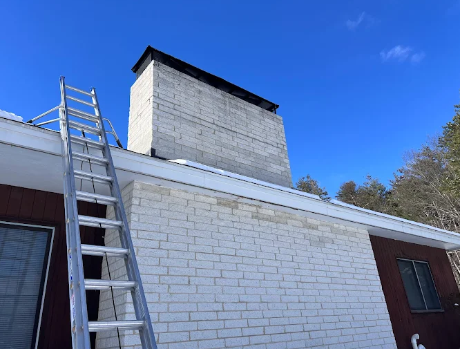 Ladder leaning against a house with a chimney and a blue sky.