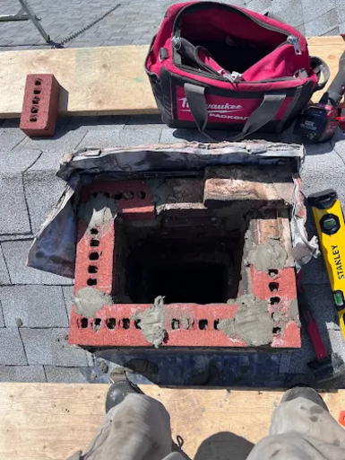 Top-down view of brick chimney repair in progress on residential roof, showing fresh mortar application and professional masonry tools during chimney restoration in Londonderry, NH.