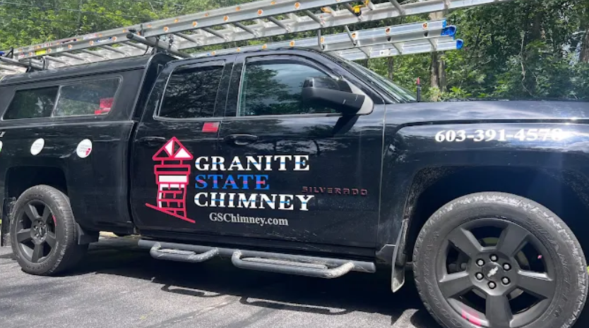 Black utility truck with logo and text on the door for Granite State Chimney, featuring a red chimney with a lighthouse, and a ladder graphic. The truck has a ladder on top and black wheels.