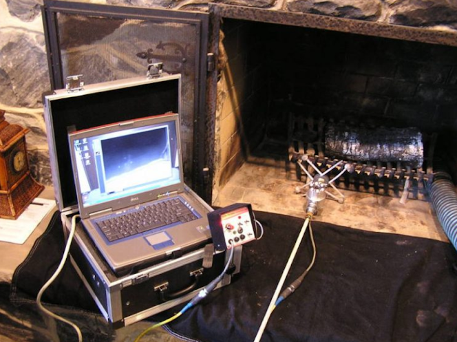 A laptop connected to scientific equipment placed near a fireplace, with one device emitting a small fire or sparks.