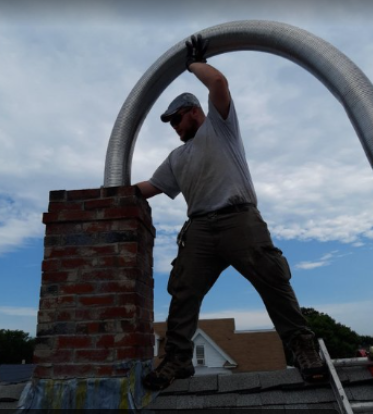 A man wearing a hat and gloves working on a roof, using a large hose or pipe.