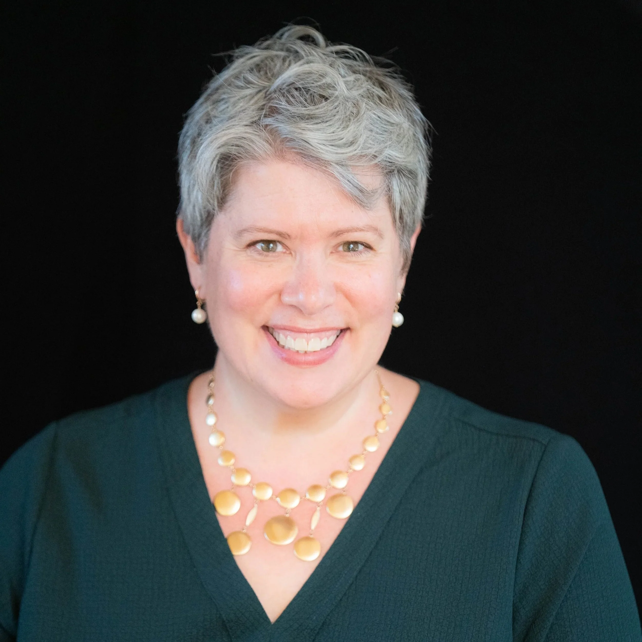 A pale woman with gray hair and a big smile looks into the camera