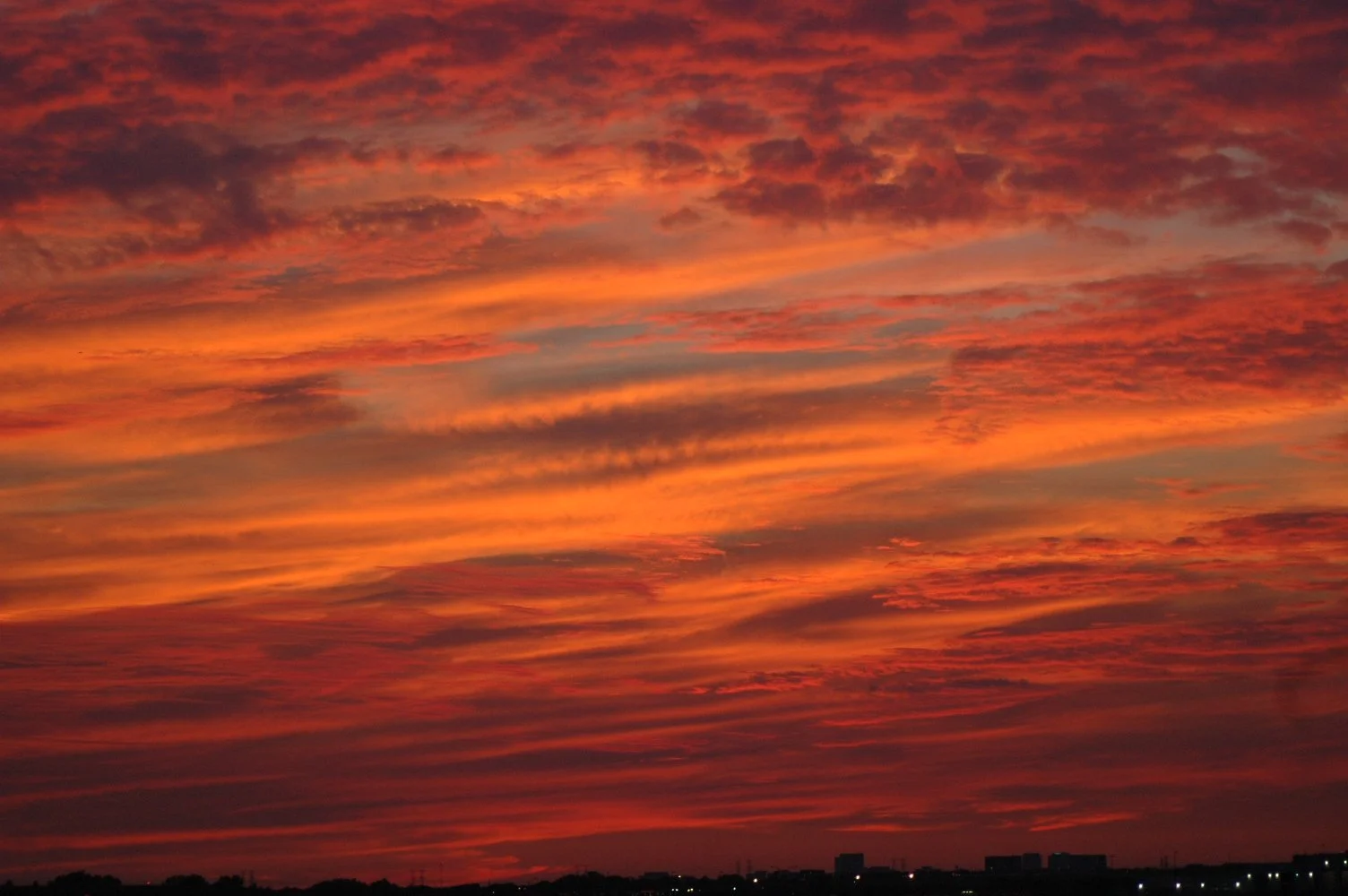 Vivid sunset sky with orange, pink, and purple clouds over a distant cityscape.