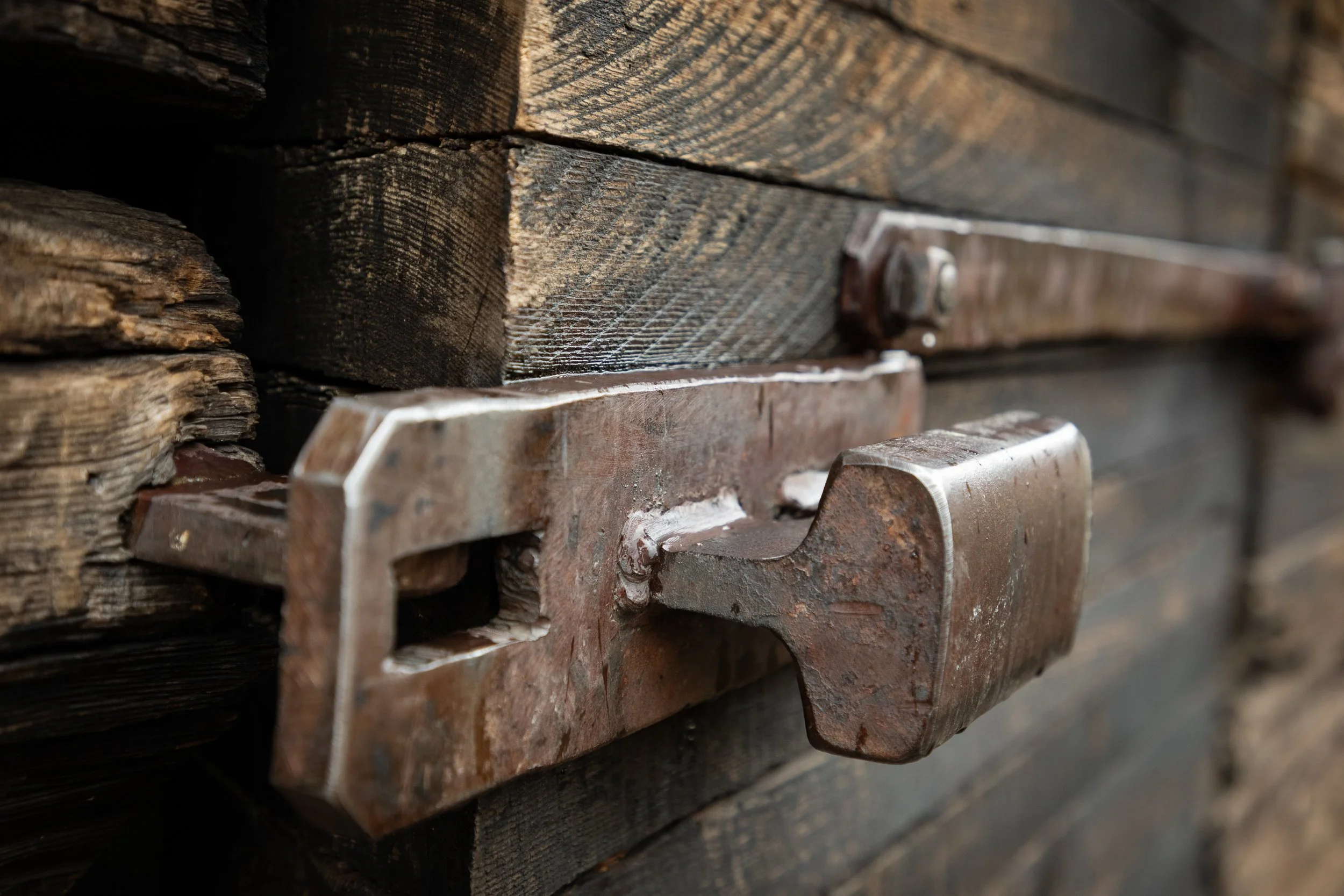 Close-up of weathered wooden planks and rusted metal L-brackets fastened with bolts.