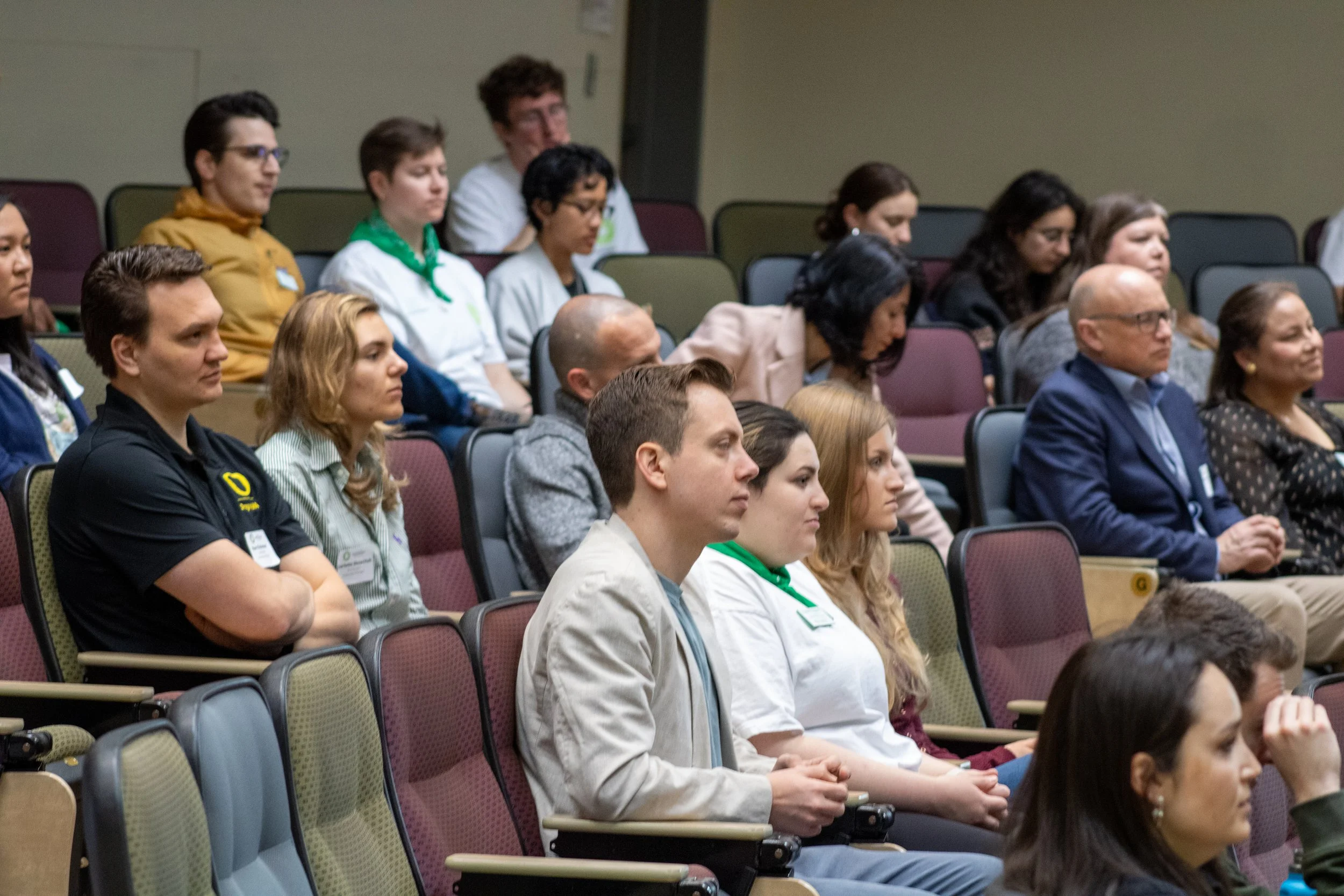Audience sitting attentively in a conference room, listening to a presentation.