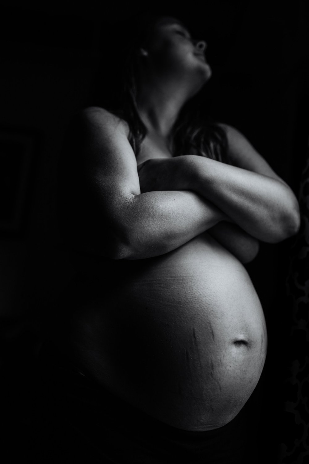 mother stands pregnant showing stretch marks and third trimester belly