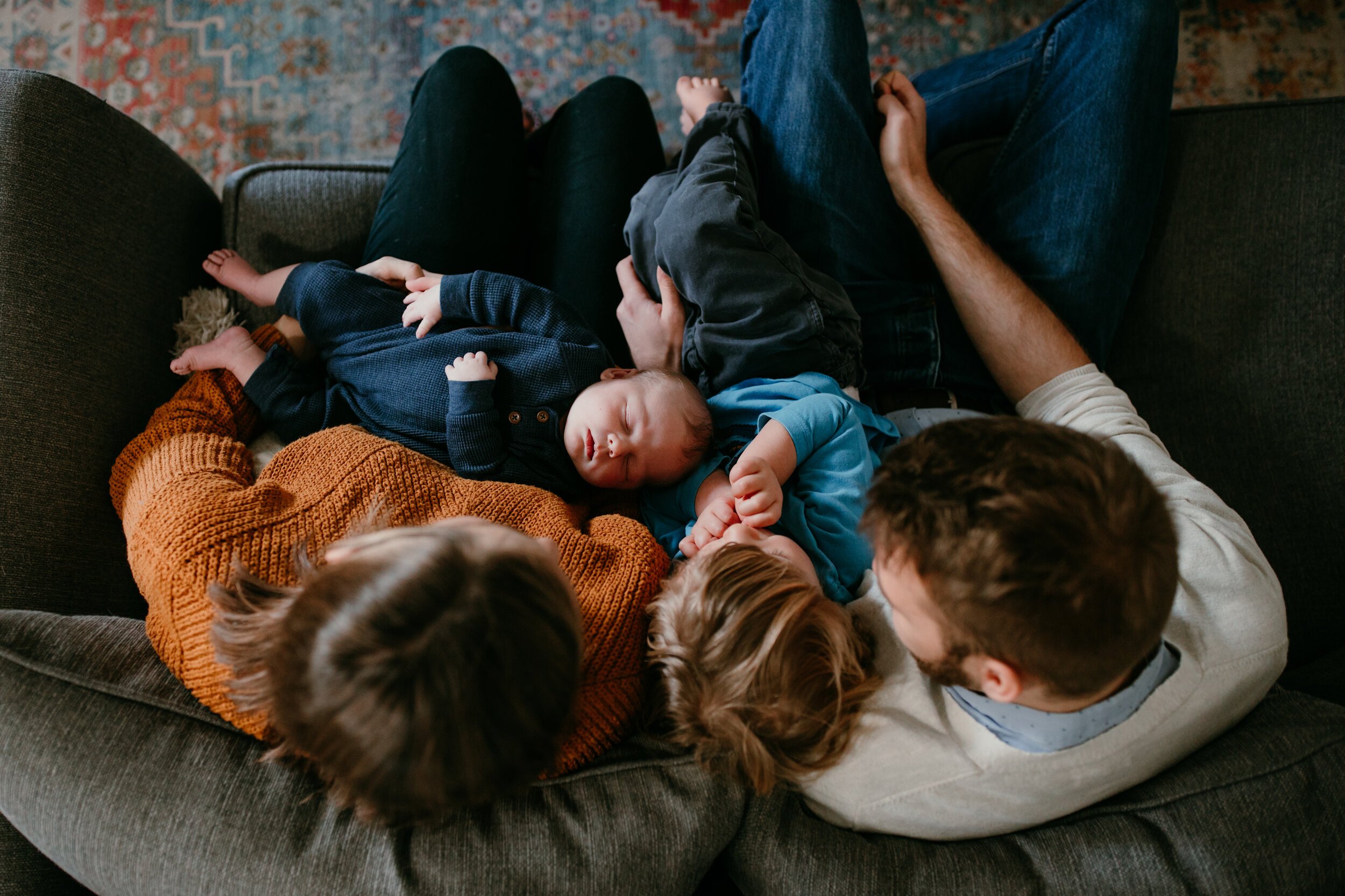 looking down on family of four on couch adoring newborn baby 